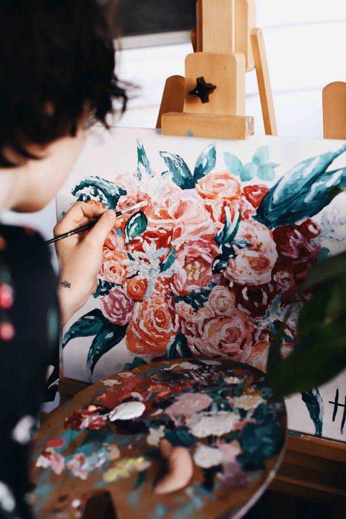 Person painting flowers and leaves with acrylic paint on canvas on an easel